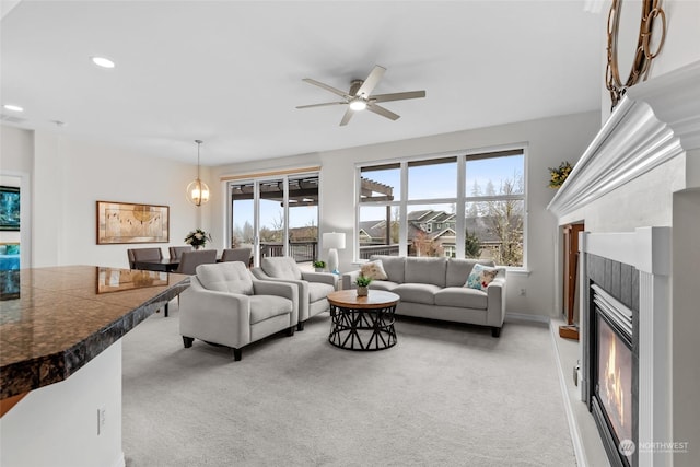 carpeted living room with ceiling fan with notable chandelier and a fireplace