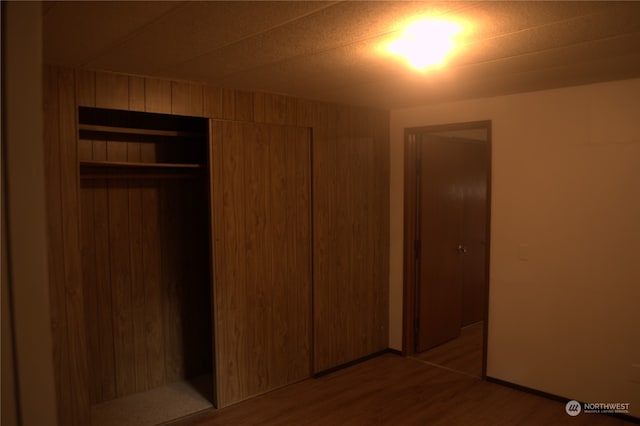 unfurnished bedroom with wood-type flooring, a closet, and wooden walls