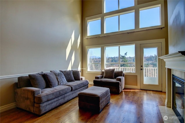 living room featuring wood-type flooring, a towering ceiling, and a tiled fireplace