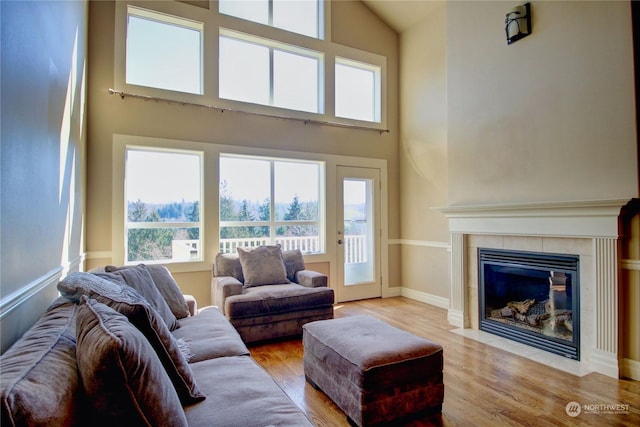 living room with a tile fireplace, a towering ceiling, and light wood-type flooring