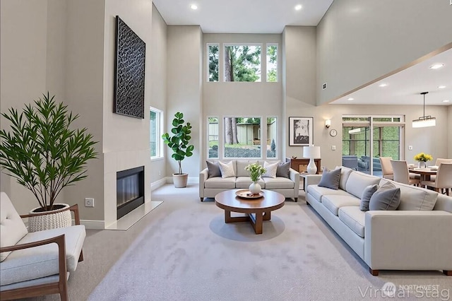 carpeted living area featuring a towering ceiling, healthy amount of natural light, baseboards, recessed lighting, and a glass covered fireplace