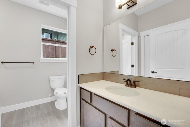 bathroom featuring toilet, tasteful backsplash, baseboards, vanity, and wood finished floors