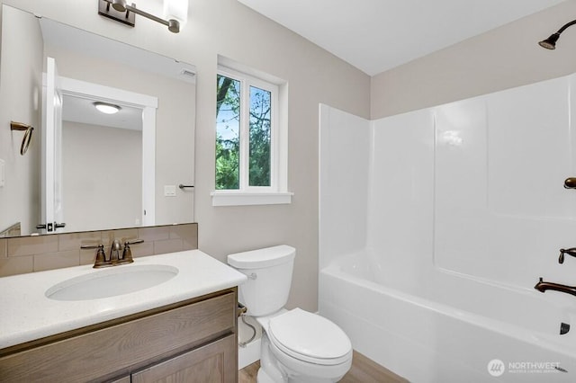 full bath featuring toilet, vanity, shower / washtub combination, and decorative backsplash