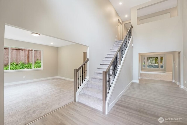 stairs featuring wood finished floors, a towering ceiling, baseboards, and recessed lighting