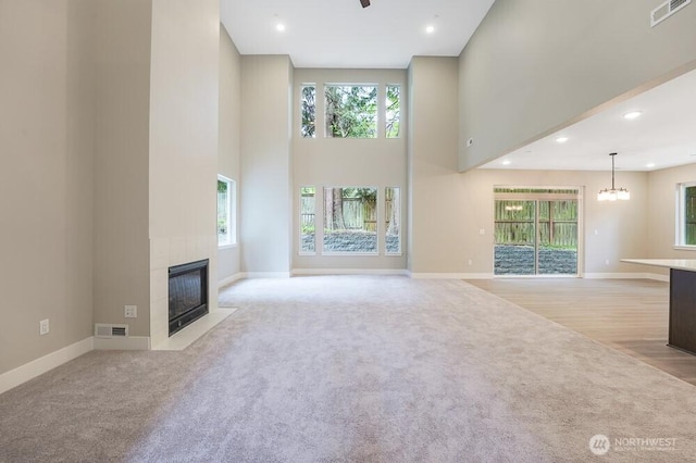 unfurnished living room with a towering ceiling, light carpet, a fireplace, baseboards, and recessed lighting