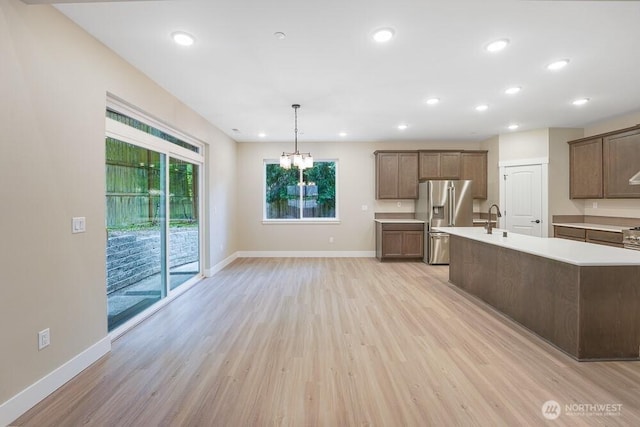 kitchen with stainless steel refrigerator with ice dispenser, light countertops, light wood-style floors, baseboards, and recessed lighting