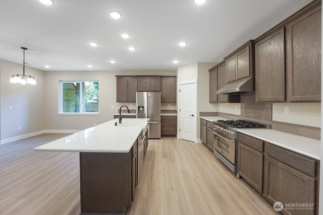 kitchen featuring stainless steel appliances, under cabinet range hood, light wood-type flooring, a sink, and light countertops
