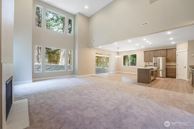 unfurnished living room with light carpet, a high ceiling, a fireplace with raised hearth, baseboards, and recessed lighting