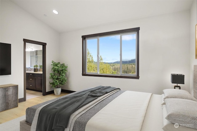 bedroom with vaulted ceiling, ensuite bath, and light wood-type flooring