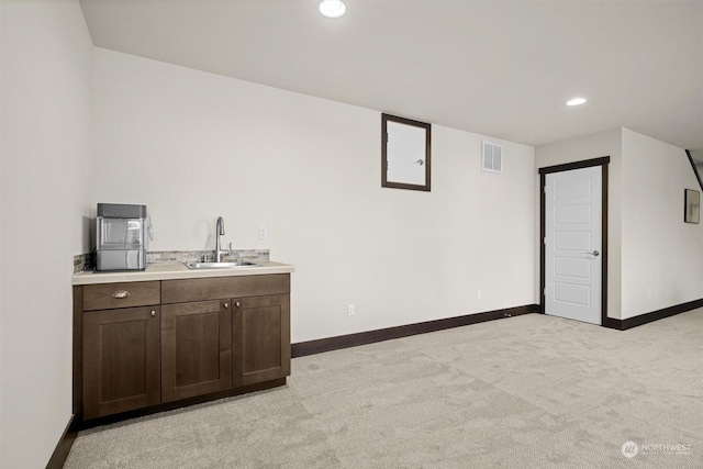 bar featuring sink, dark brown cabinets, and light carpet