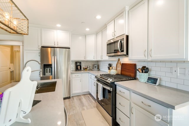 kitchen with backsplash, light wood-type flooring, stainless steel appliances, decorative light fixtures, and white cabinets