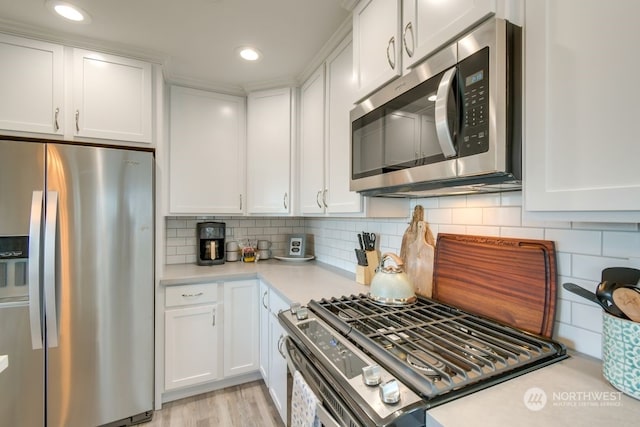 kitchen featuring backsplash, white cabinets, light wood-type flooring, and appliances with stainless steel finishes