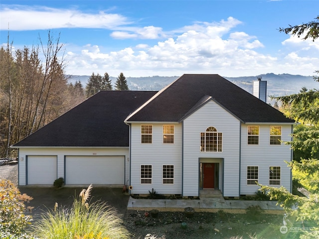 colonial home featuring an attached garage, a mountain view, and a chimney