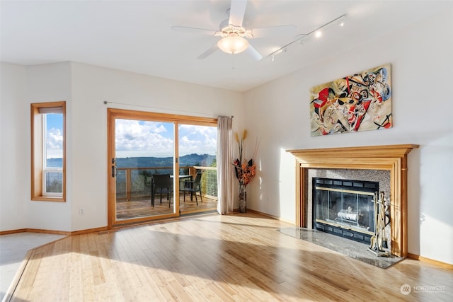 unfurnished living room with a premium fireplace, baseboards, wood finished floors, and a ceiling fan