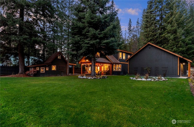 back house at dusk featuring a lawn and an outdoor structure