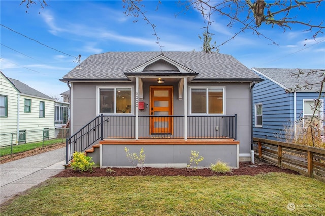 bungalow-style home with a front yard, fence, roof with shingles, and stucco siding