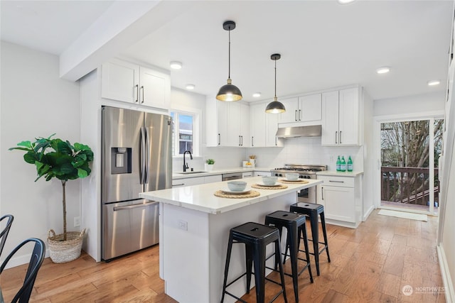 kitchen with under cabinet range hood, a sink, tasteful backsplash, appliances with stainless steel finishes, and light wood finished floors