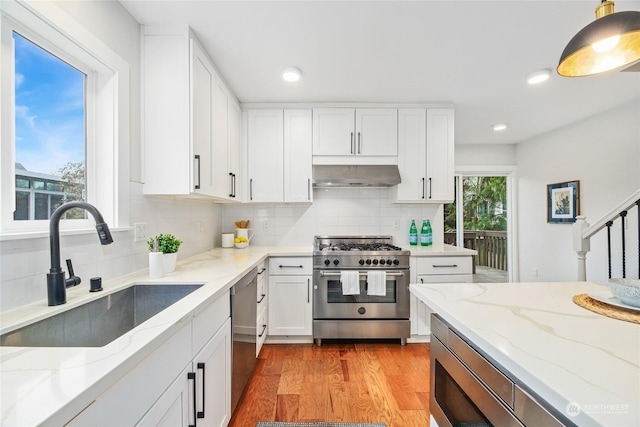 kitchen featuring under cabinet range hood, a sink, backsplash, light wood-style floors, and appliances with stainless steel finishes