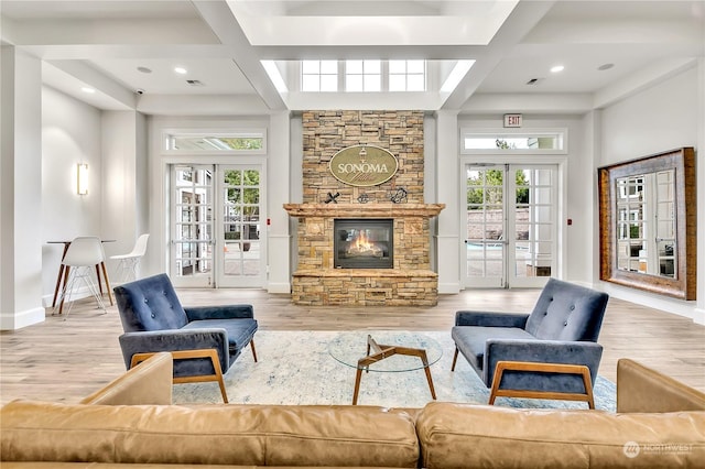 living room featuring coffered ceiling, a stone fireplace, hardwood / wood-style flooring, and french doors