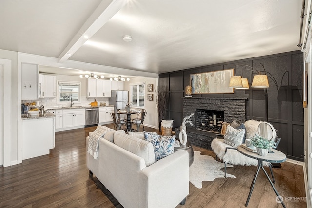 living room with beamed ceiling, dark hardwood / wood-style floors, a stone fireplace, and sink