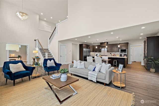 living room featuring light wood-type flooring, a chandelier, and a high ceiling