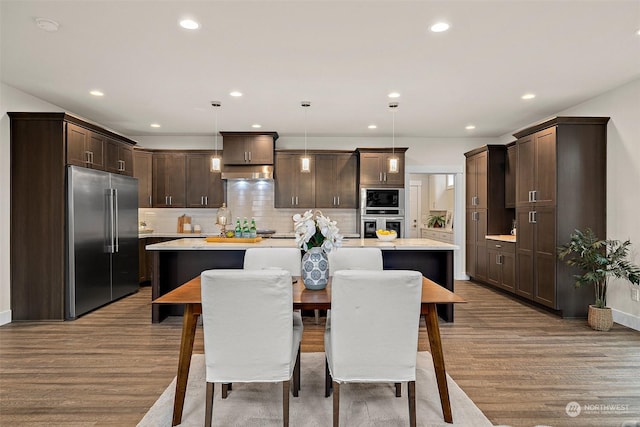 kitchen featuring wood-type flooring, hanging light fixtures, a center island with sink, and built in appliances