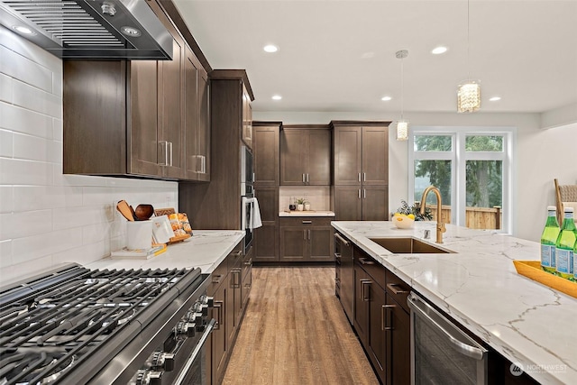 kitchen with dark brown cabinetry, stainless steel appliances, sink, hanging light fixtures, and ventilation hood