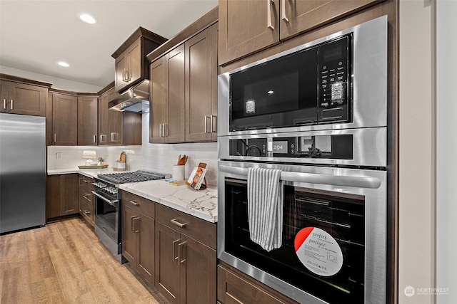 kitchen with dark brown cabinetry, built in appliances, decorative backsplash, light stone counters, and light hardwood / wood-style flooring