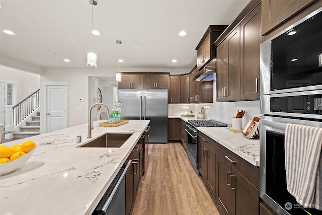 kitchen with dark brown cabinetry, decorative light fixtures, built in appliances, sink, and light hardwood / wood-style flooring