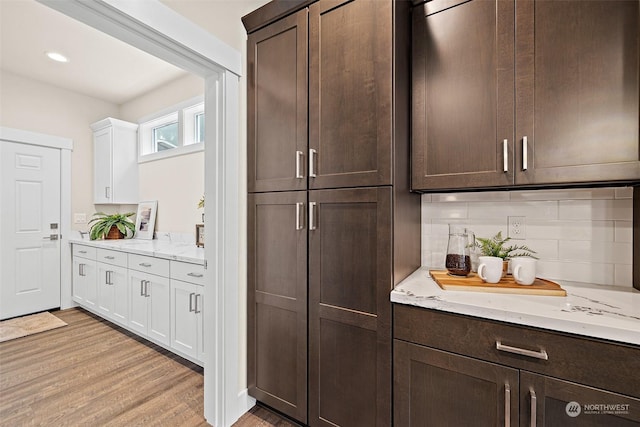 bar with light hardwood / wood-style floors, backsplash, white cabinets, and dark brown cabinets