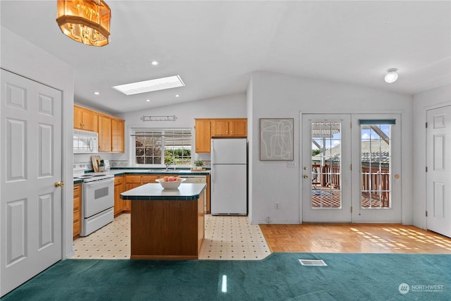 kitchen with light carpet, vaulted ceiling with skylight, white appliances, a center island, and hanging light fixtures