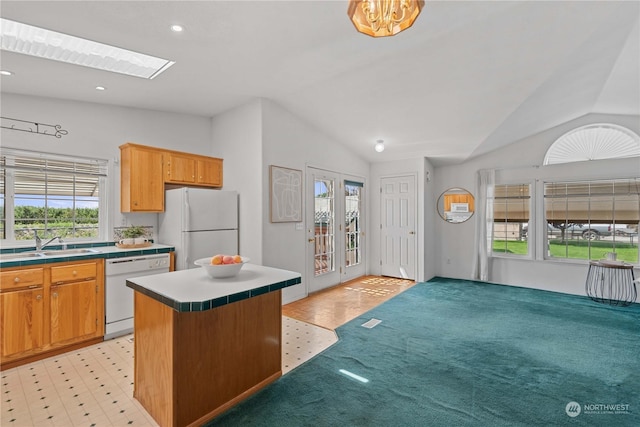 kitchen with white appliances, a kitchen island, lofted ceiling with skylight, and sink