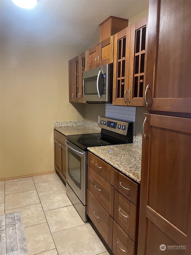 kitchen with backsplash, light stone counters, light tile patterned floors, and appliances with stainless steel finishes