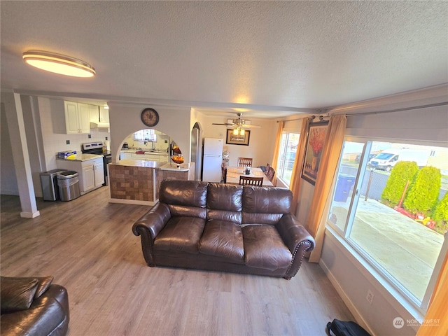 living room with ceiling fan, a textured ceiling, and light wood-type flooring