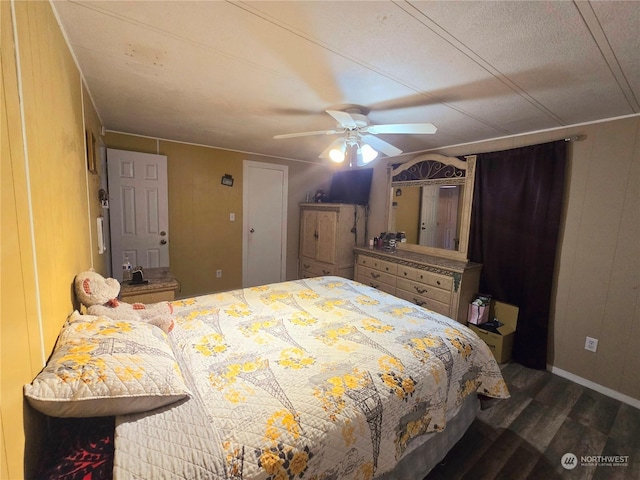 bedroom featuring dark hardwood / wood-style flooring, ceiling fan, and wooden walls