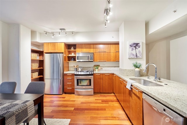 kitchen with sink, light stone countertops, light hardwood / wood-style flooring, and appliances with stainless steel finishes