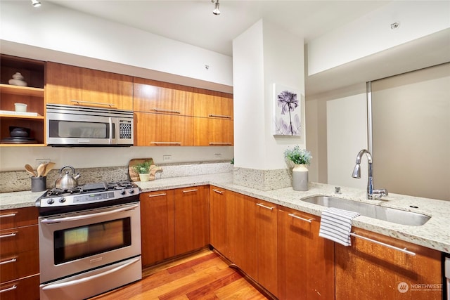 kitchen with stainless steel appliances, sink, light hardwood / wood-style floors, and light stone countertops