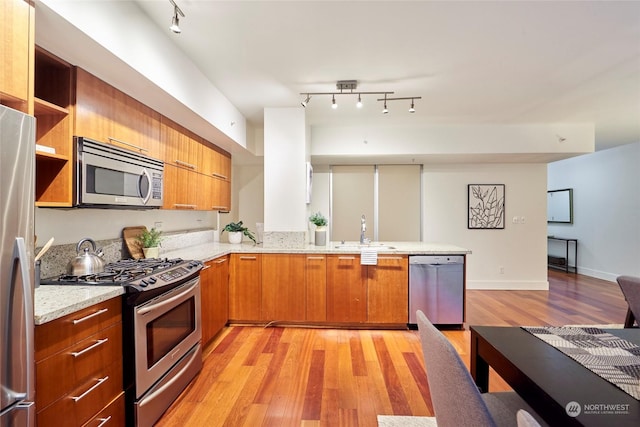 kitchen featuring kitchen peninsula, appliances with stainless steel finishes, light stone countertops, and sink