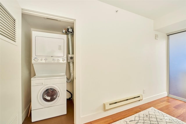 laundry area featuring hardwood / wood-style flooring, a baseboard radiator, and stacked washer / dryer