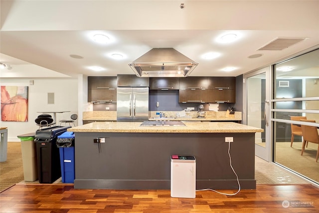 kitchen with light stone countertops, a breakfast bar, stainless steel fridge, dark wood-type flooring, and exhaust hood