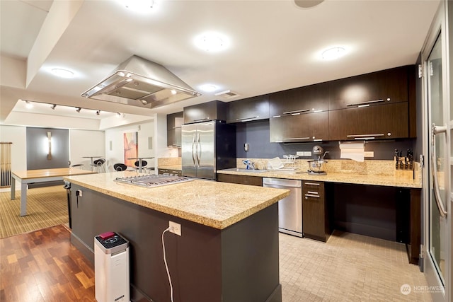 kitchen featuring island exhaust hood, appliances with stainless steel finishes, light stone counters, a kitchen island, and dark brown cabinets