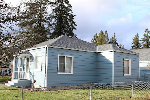 view of side of property with a shingled roof, a yard, and fence