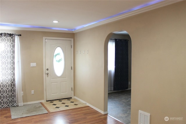 entryway with visible vents, arched walkways, wood finished floors, and ornamental molding