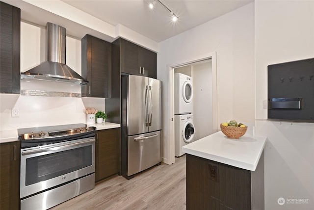 kitchen featuring dark brown cabinetry, stainless steel appliances, stacked washer / drying machine, and wall chimney exhaust hood