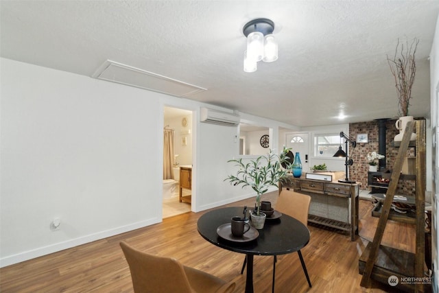 dining space featuring wood-type flooring, a textured ceiling, a wood stove, and a wall mounted AC