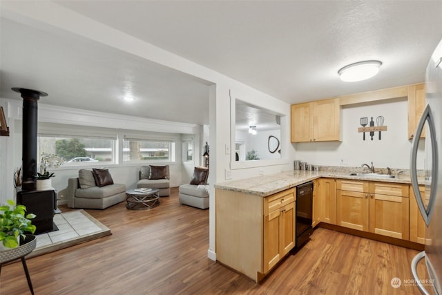 kitchen featuring a wood stove, light stone counters, black dishwasher, light brown cabinetry, and stainless steel refrigerator