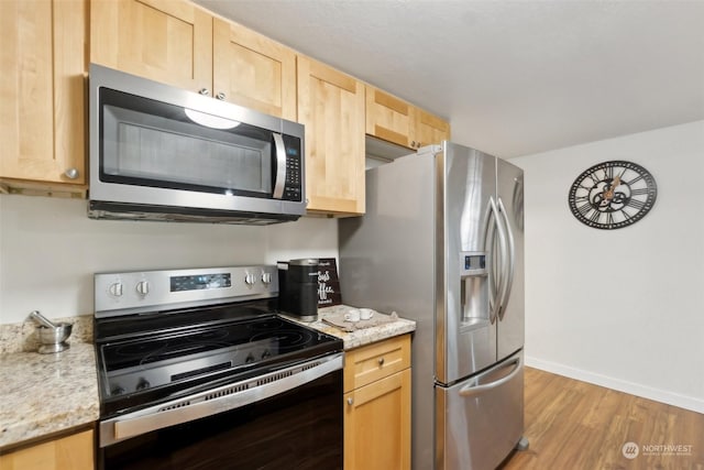 kitchen with stainless steel appliances, light brown cabinets, light wood-type flooring, and light stone countertops