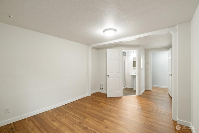 unfurnished bedroom with a textured ceiling, light wood-type flooring, and ensuite bathroom