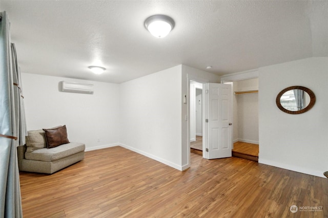 living area with a textured ceiling, hardwood / wood-style floors, and a wall unit AC