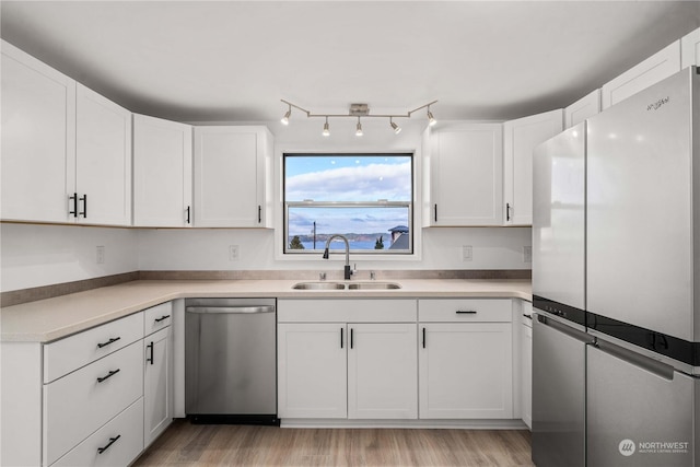 kitchen with appliances with stainless steel finishes, white cabinetry, light wood-type flooring, and sink